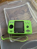 Photo of a green My Arcade handheld game console with a directional pad on the left, buttons on the right, and a wrist strap connected on the left side.