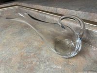 Clear glass jug with a long neck, rounded bulbous base, and attached curved handle shown on a countertop