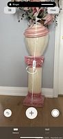 Large cream and pink decorative vase on matching pedestal with fluted column and Ionic detail.