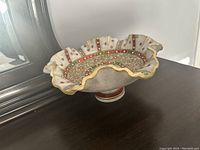Photo showing a marble decorative bowl with ruffled edges and colorful paint accents in gold, red, and green placed on a surface near a mirror.
