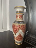 Photo showing a decorative marble vase with detailed gold, red, blue, and white designs placed near a mirror on a dark surface, capturing the front and side of the vase.