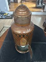 Front view of the brown metal lantern with the door open showing the candle inside on a black surface