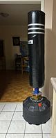 Front view of black vinyl punching bag on blue stand with fillable base in living space