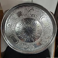 Top-down photo showing the large silver serving dish with intricate floral and scroll engravings and central sunburst pattern.