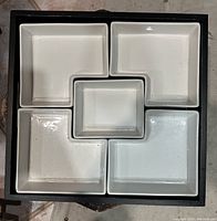 Top-down view of black serving tray with five white ceramic compartments arranged within.