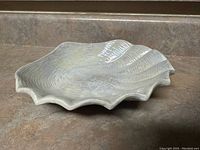 Photo of a single decorative bowl shaped like a clam shell with ridged texture and pearlescent finish