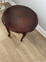 Top view showing round scalloped tabletop with dark brown wood finish and some paint chips around the edge.