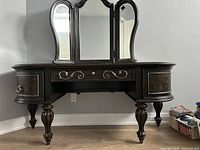 Front view of dark wood vanity dresser with three attached folding mirrors and curved legs