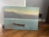Canvas painting showing a lake with a wooden dock and a single red canoe in calm water, misty mountains in background.