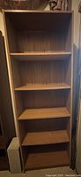 Front view of tall wooden bookshelf with five shelves and wood grain finish.