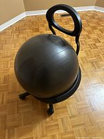Front angle view of the yoga ball mounted in the rolling base with backrest on a parquet floor.