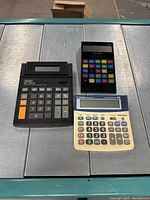 Three calculators placed side by side on a metallic surface showing front face and keys.