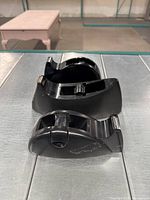 Photo of three black plastic tape dispensers placed on a metal surface, showing different shapes and metal cutting blades.