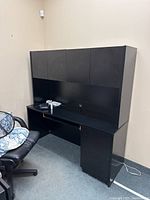 Black wooden credenza with upper cabinets and a work surface with some scratches, taken from a front angle showing the entire piece including cable management hole.