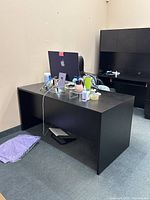 Front and side view of the black wooden desk, showing its rectangular shape and smooth black finish. Desk has no drawers or attachments. Minor surface wear visible.