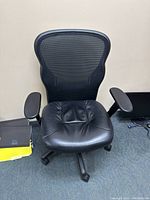 Front view of black office chair showing leather seat and mesh backrest.