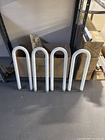 Four U-shaped white fluorescent light bulbs leaning against a wall with cardboard box background.