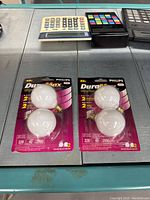 Two packs of Philips DuraMax frosted globe light bulbs on display with calculators in the background
