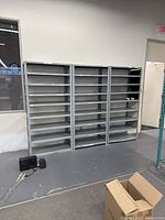 Front view showing three gray metal shelving racks mounted against wall