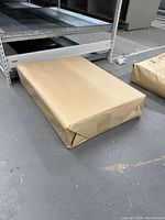 Package of packing paper sheets wrapped in brown paper on a warehouse floor near shelving