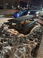 Outdoor weathered wooden picnic table with bench seating covered in snow, showing use wear and scraping on wood surface.