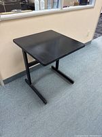 Full view of small black table showing rectangular top and metal frame base against beige wall and carpeted floor