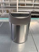 Front view showing shiny stainless steel body with push-to-open lid and SimpleHuman branding on lid.