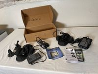 Two Garmin GPS devices laid out with their car suction cup stands, power chargers, and instruction manuals arranged on a table next to an open cardboard box labeled '2 Garmin'.