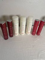 Full view of seven skincare bottles arranged in a row on a cloth surface: three white m-body lotions, two red m-press day moisturizers, and two red m-merse night creams.