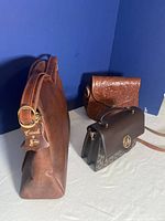 Three vintage leather purses arranged side by side on a blue background, showing shape and color contrast.