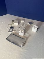 Full lot display showing iPod, two earbuds sets in cases, chargers, cables and clear iPhone case on white surface against blue background.