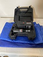 Black & Decker rotary tool and power unit in black carrying case on top of two folded blue tarps.