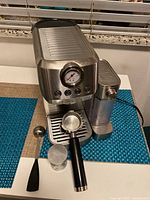 Angled front view showing espresso maker, pressure gauge, milk steamer, portafilter, tamper and spoon
