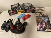 Overall view of the lot showing 7 alloy model cars in various packaging and loose, 3 PlayStation 2 video games, and 2 sets of Motorola walkie talkies with charging station and power adapter.