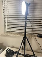 LED photo light turned on, mounted on black tripod stand in a room setting