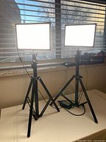 Two GVM Raleno LED photo lights mounted on tripods, both lights turned on emitting bright white light by window.