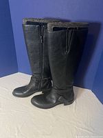 Side angle view of tall black horseback riding boots showing zipper and buckle details.