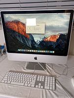 Full view of Apple iMac with keyboard and mouse, showing screen with OS X El Capitan desktop.