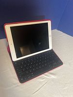 Apple iPad with white bezel and black screen, mounted upright on a red keyboard case with black keys.