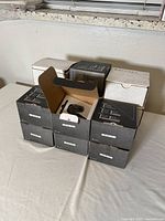 Stack of 15 black and white boxes, each containing one security camera. One box is open revealing the camera inside.