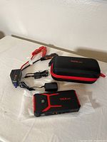 Tack Life battery charger and jump starter device with carrying case, clamps, and chargers arranged on flat surface.