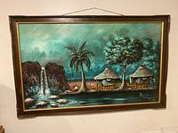 Full view of the framed tropical countryside painting with huts by a water body, showing the waterfall, trees, and serene environment.