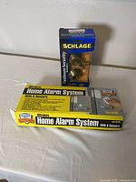 Photo showing original packaging of Schlage door deadbolt lock and boxed wireless home alarm system