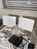 Photo of two Square iPad POS stands with power cables, black charging station with six ports, Vagaro credit card reader, and multiple white power cords including three extension cords.