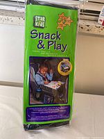 Photo of the original packaging for a Star Kids Snack & Play Travel Tray showing product branding, product name, and a child using the tray in a car seat.