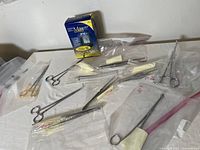 Photo showing 10 metal surgical tools individually bagged and an Accu-Chek Aviva glucose monitor box on a white surface.
