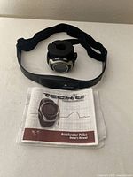 Tech 4O Accelerator Pulse Series wristwatch, heart rate monitor chest strap, and owner's manual displayed on white surface.