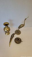 Overview of all four brass items: vase, giraffe figurine, candle holder, and parrot figurine on white background