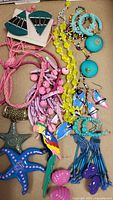 Bright assorted costume jewelry photo showing colorful beaded necklaces, multiple pairs of earrings in turquoise, pink, purple and blue, and starfish brooches.