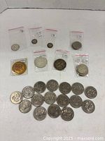 Coins displayed showing some in plastic sleeves including 1858-1958 commemorative dollar, various other coins spread out on white surface.